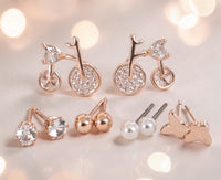 SOVAR five-pair earrings collection with bicycle, clear stone, gold-tone ball, white pearl-style and butterfly studs under soft lighting.