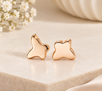Pair of polished gold-tone butterfly-shaped stud earrings displayed on beige stone beside white flowers.