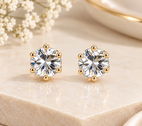 Pair of round clear faceted stud earrings held in gold-tone six-prong settings on beige stone.