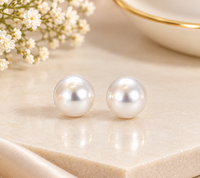 Pair of round white pearl-style stud earrings displayed on beige stone beside white flowers.